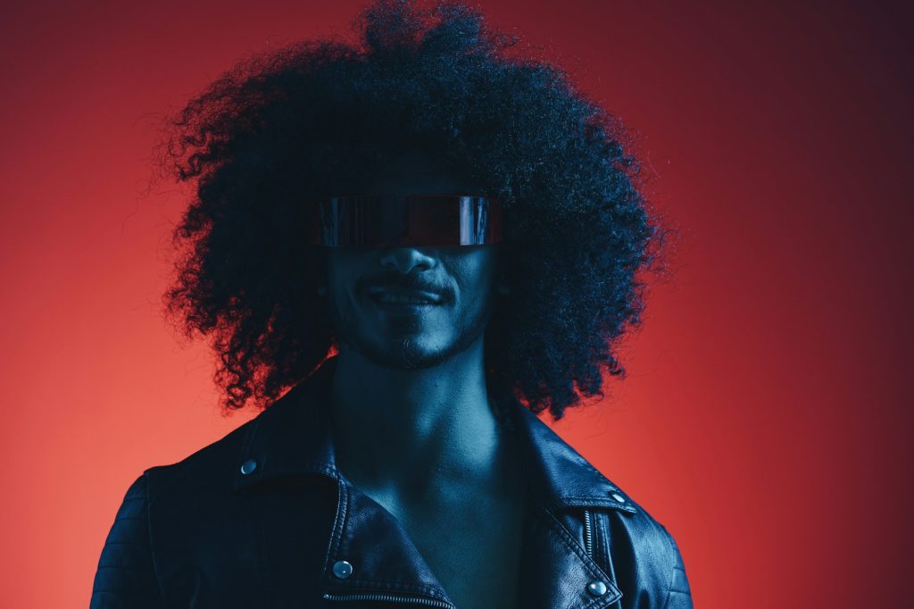 Portrait of fashion man with curly hair on red background with stylish glasses, multicultural